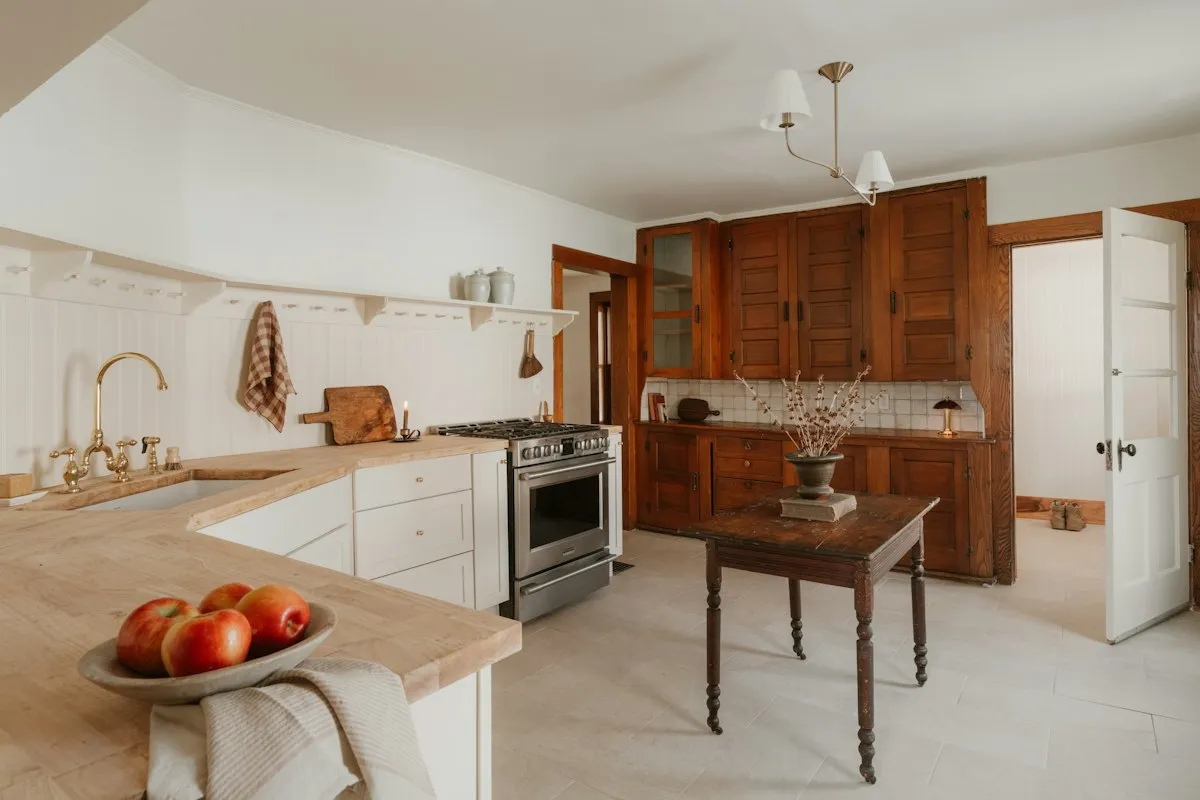 Cuisine de maison ancienne avec plan de travail en bois massif, évier sous fenêtre et buffet vitré en bois foncé au fond