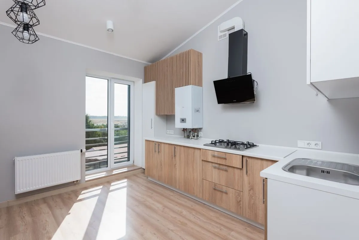 Cuisine linéaire à façades bois clair et plan blanc, avec prises murales au-dessus du plan de travail et hotte noire