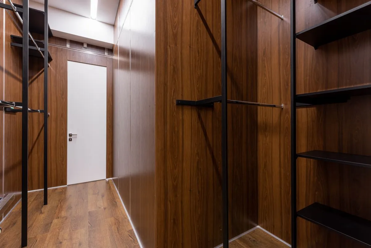 Dressing en couloir aux parois en bois foncé, étagères et tringles noires de part et d'autre d'un passage central