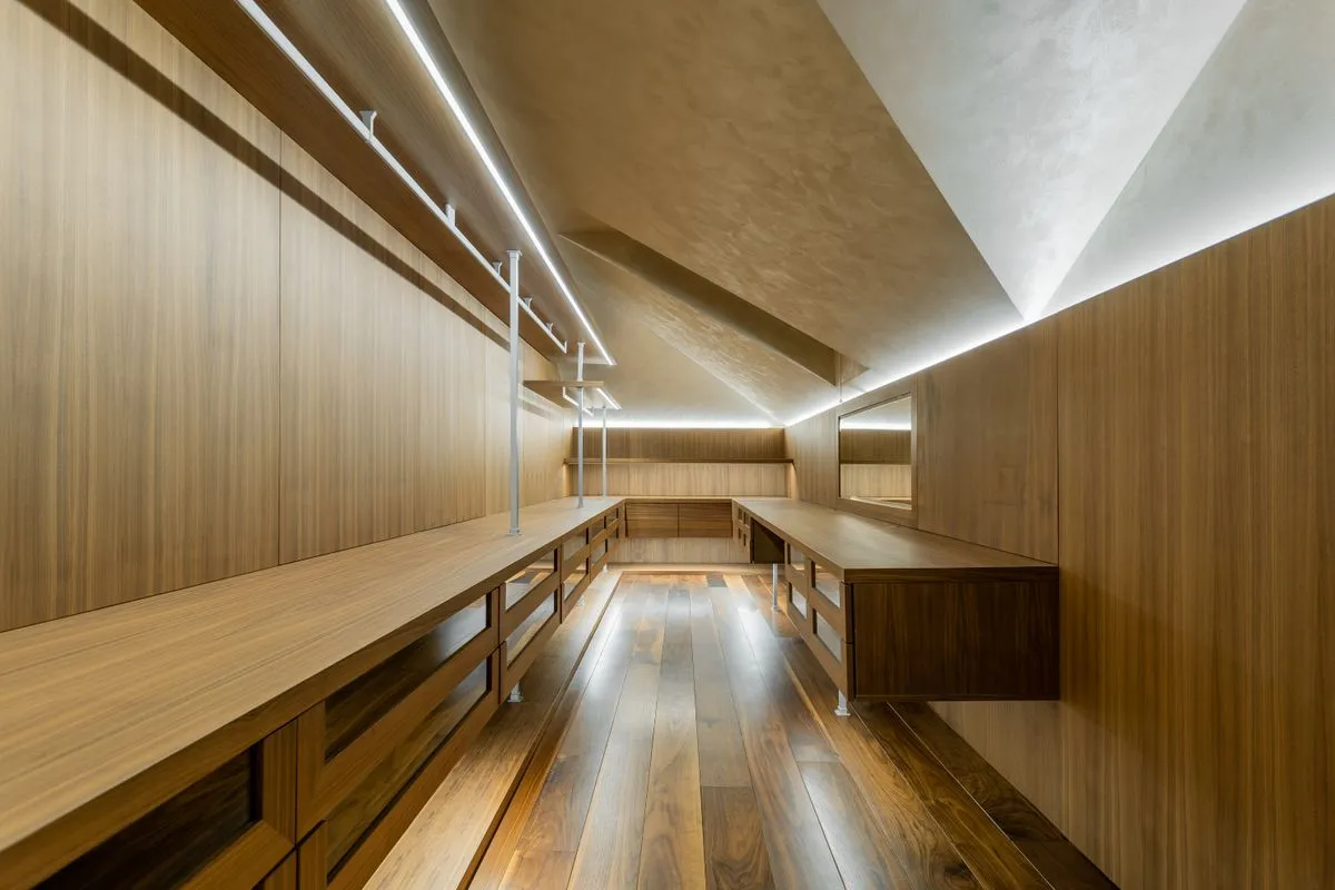 Dressing aménagé sous un plafond en pente, habillé de panneaux en noyer, avec tiroirs bas et bandeau LED le long du rampant