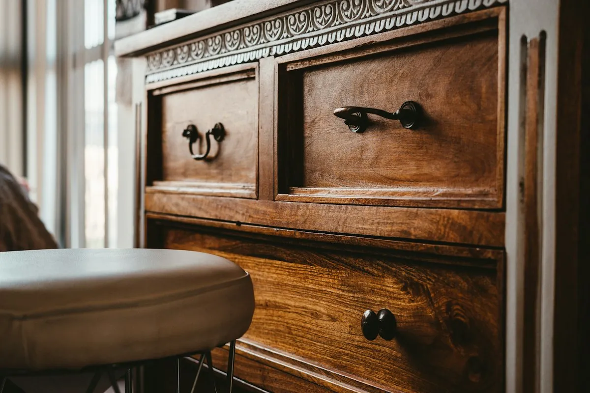 Commode ancienne en bois foncé avec frise sculptée et poignées en métal, vue de trois quarts