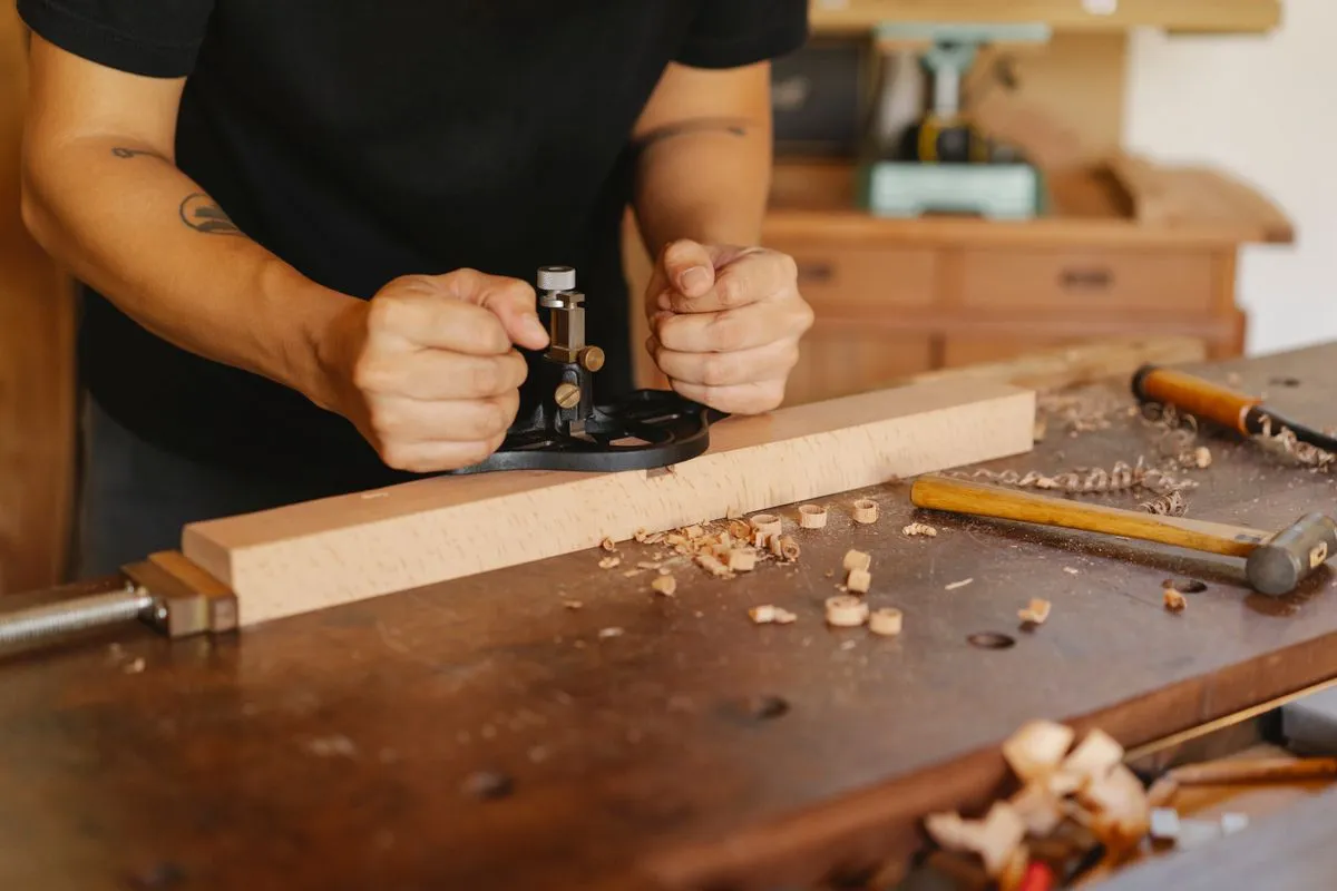Artisan rabotant une planche de bois clair au rabot à main sur un établi couvert de copeaux