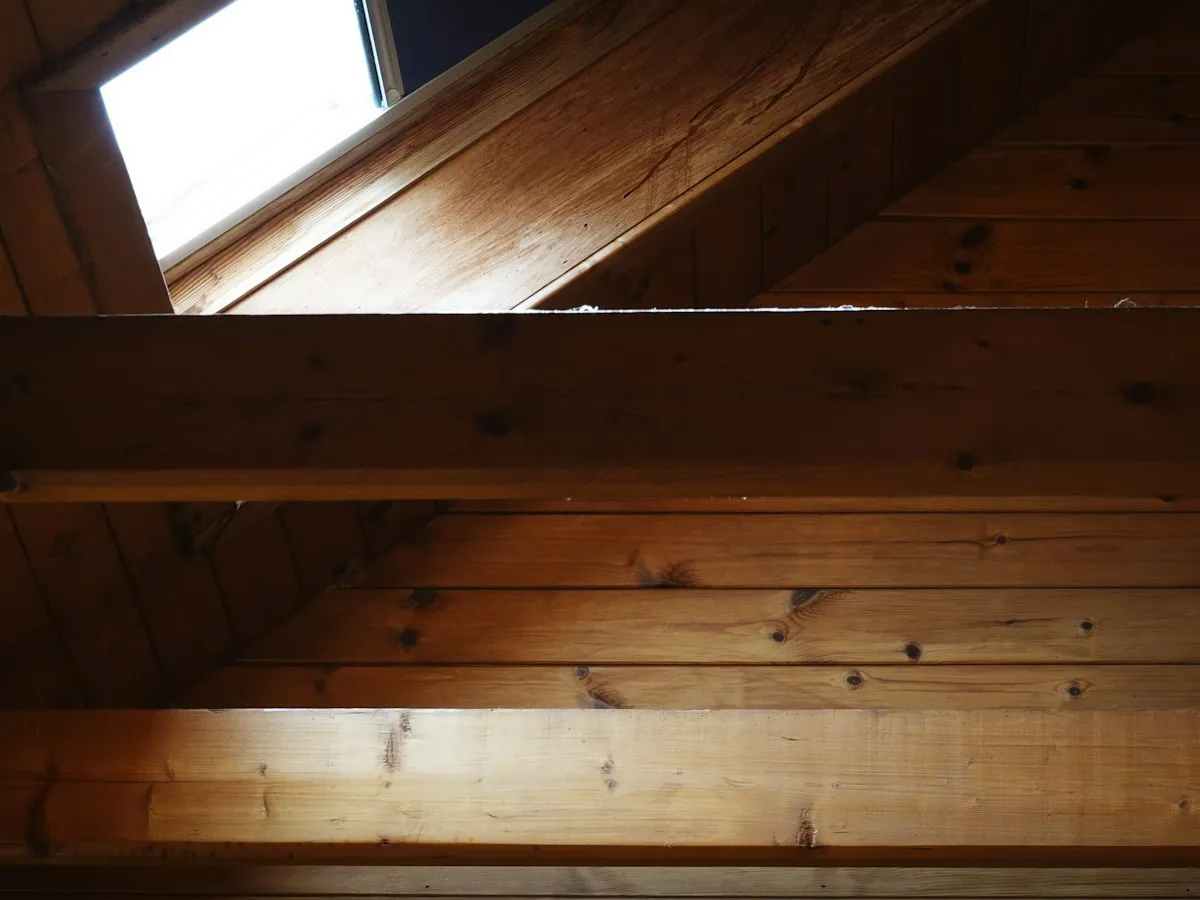Combles aménagés vus de l'intérieur, avec lambris et poutres en bois éclairés par une fenêtre de toit