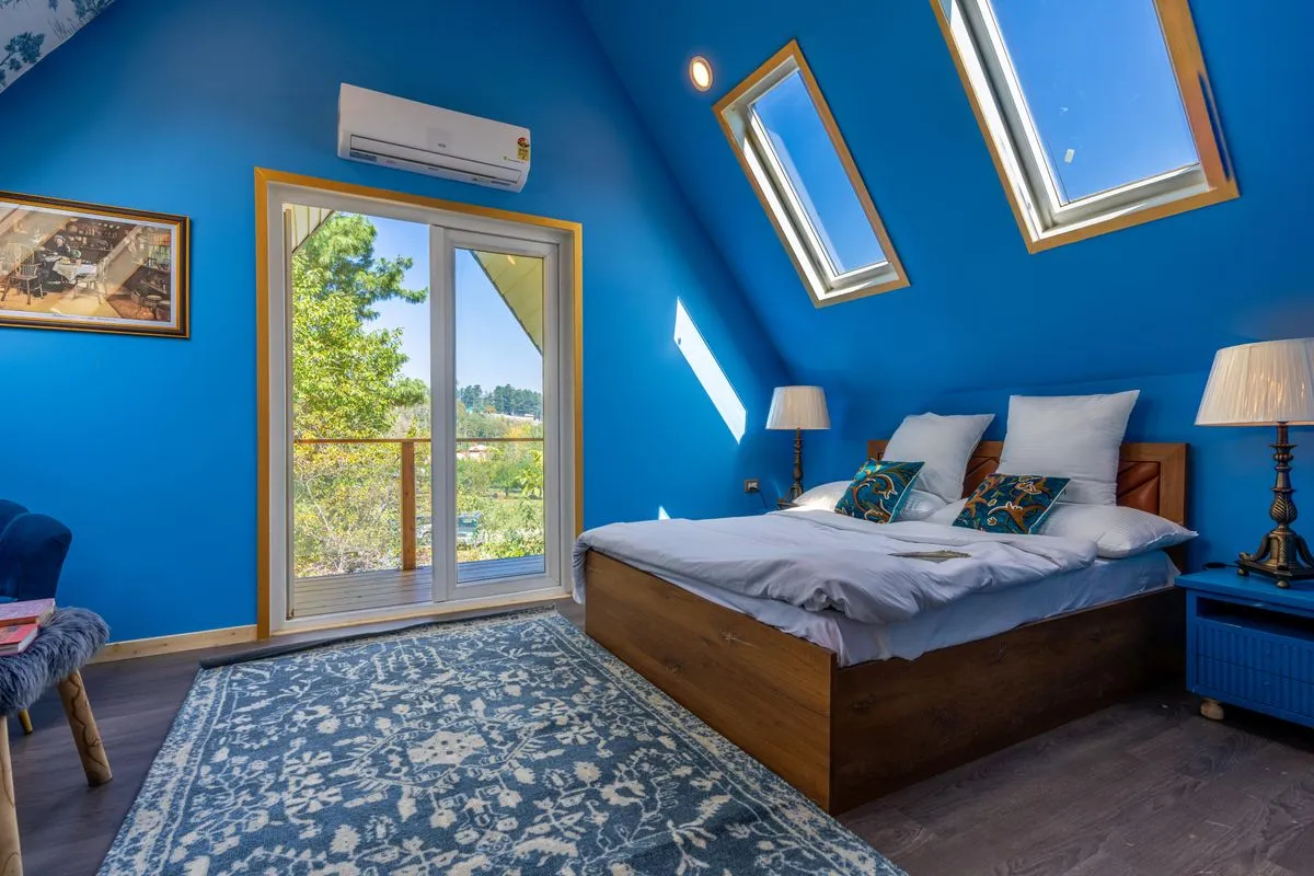 Chambre sous combles aux murs bleus, éclairée par deux fenêtres de toit à cadre bois dans le rampant