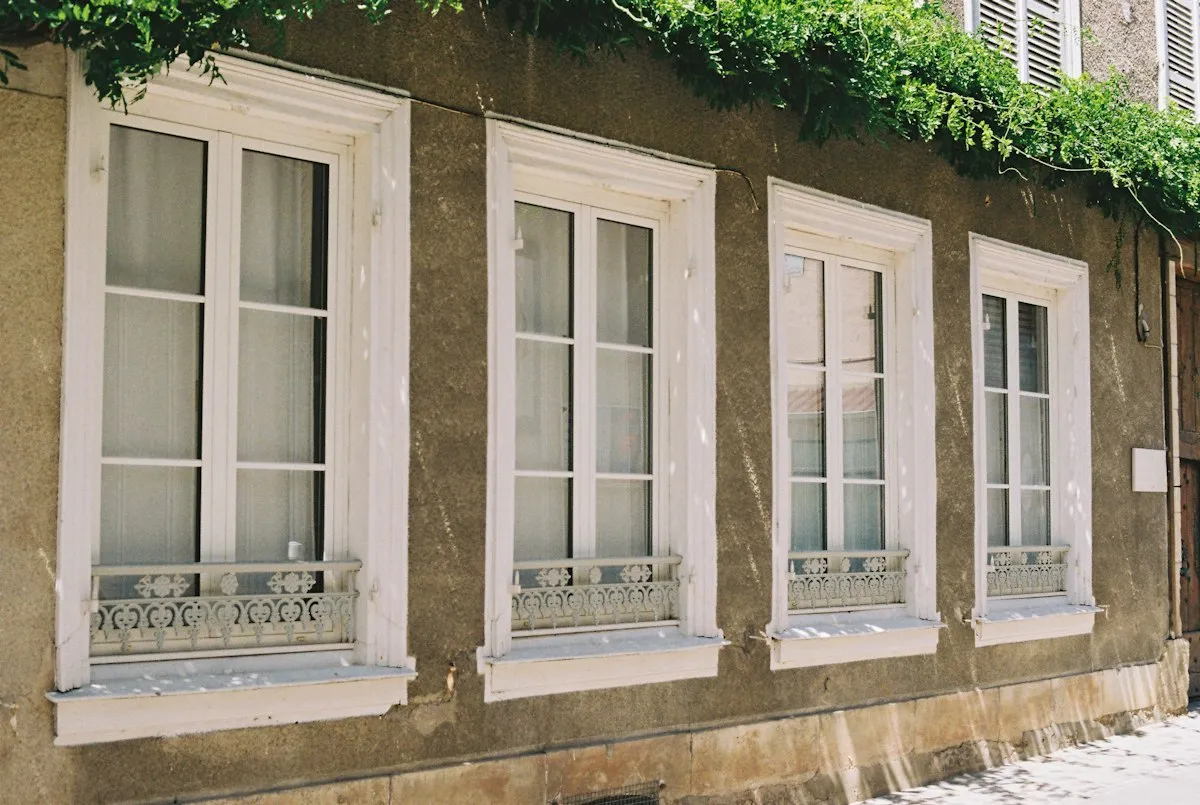 Fenêtres anciennes en bois peint blanc à petits bois, avec garde-corps en fonte, sur une façade enduite
