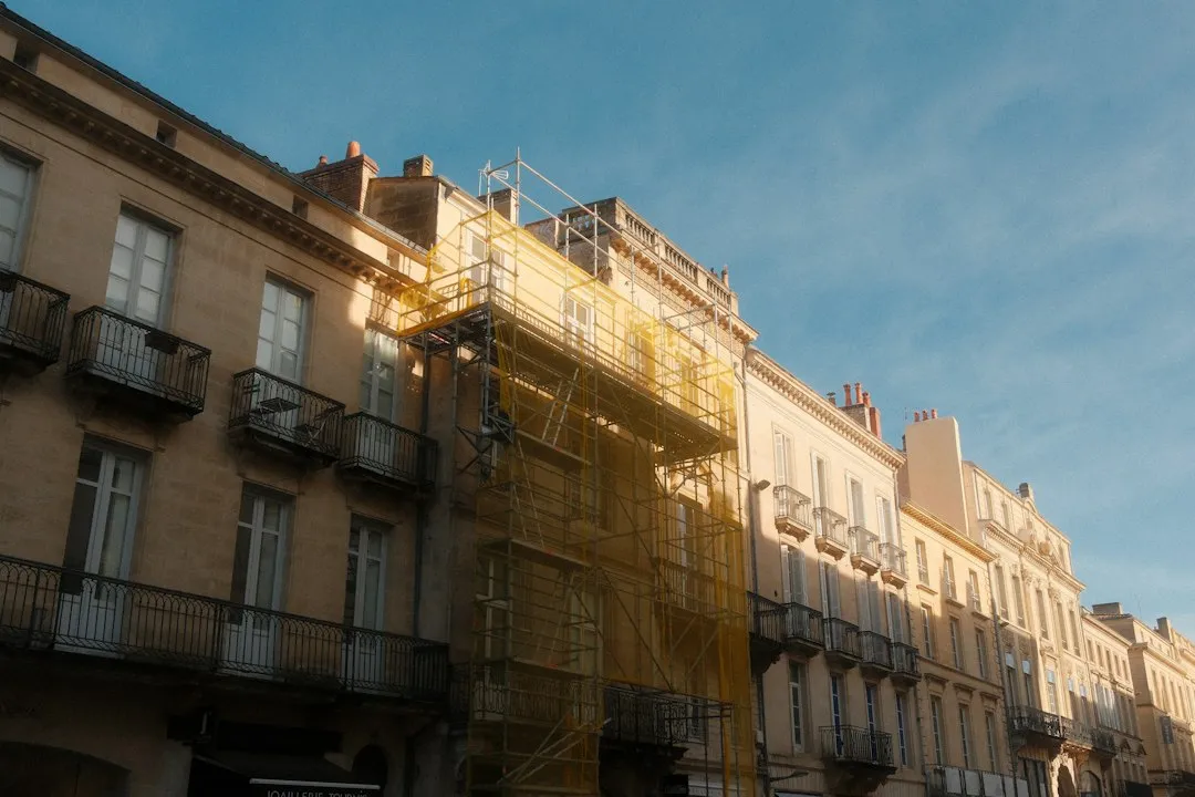 Rue d'immeubles en pierre blonde à balcons en fer forgé, dont une façade sous échafaudage pour rénovation