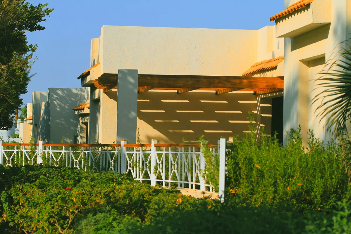 Pergola à poutres en bois adossée à une maison enduite, projetant ses ombres sur la façade