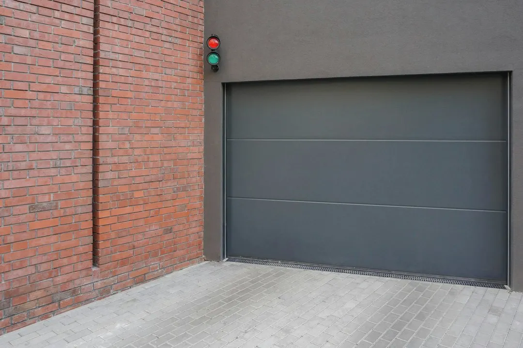Porte de garage sectionnelle grise motorisée, à panneaux lisses, avec feu de signalisation rouge et vert à côté de l'ouverture