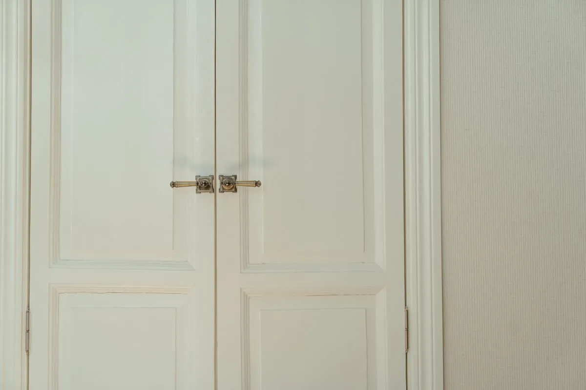 Porte intérieure à deux vantaux en bois peint blanc, à panneaux moulurés et béquilles en laiton, typique d'un appartement ancien