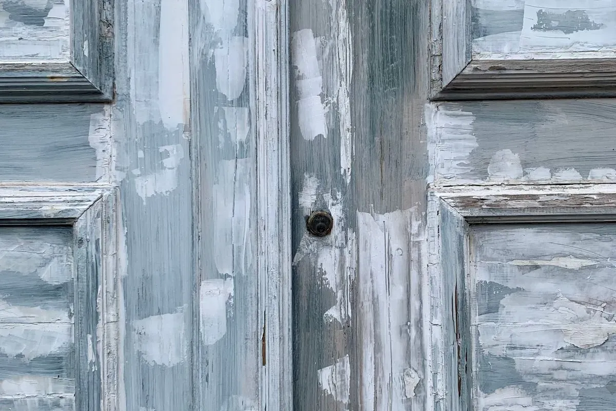 Vantaux de porte anciens à panneaux moulurés, couverts de couches de peinture gris-bleu et blanche écaillées