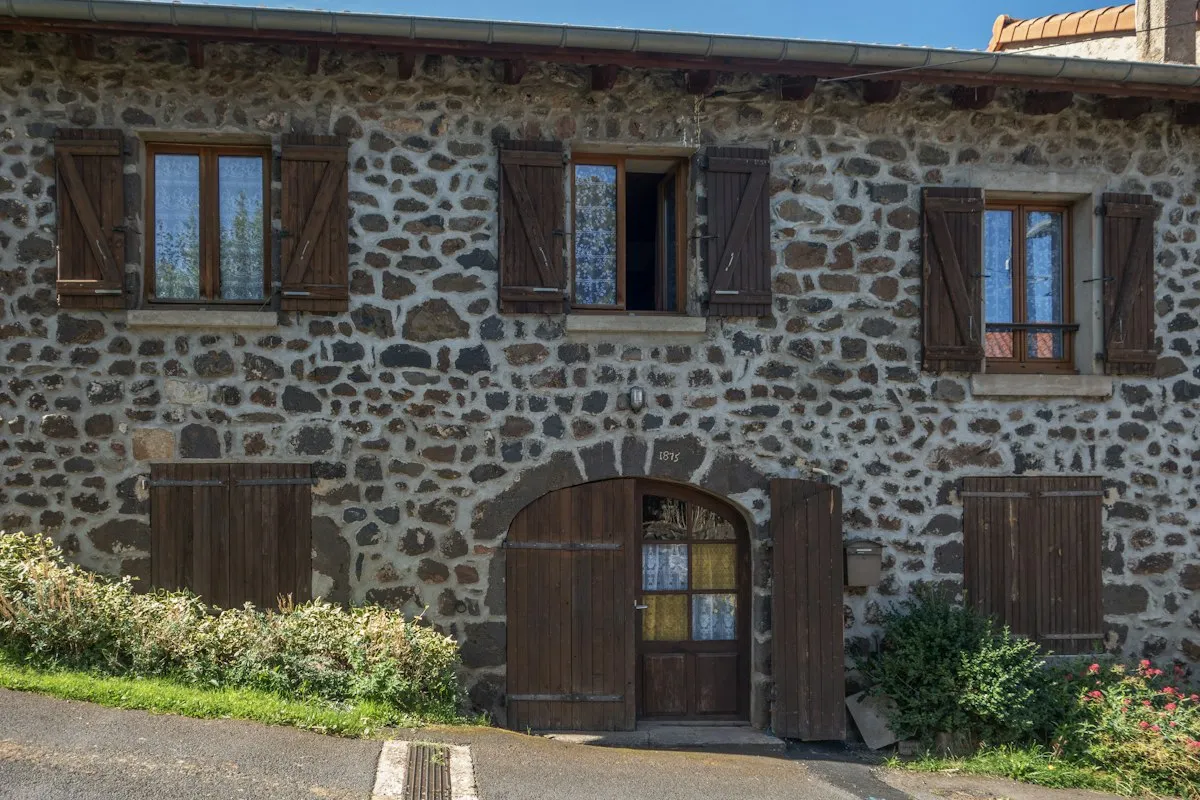Maison en pierre avec volets battants en bois brun aux fenêtres et porte cintrée en bois